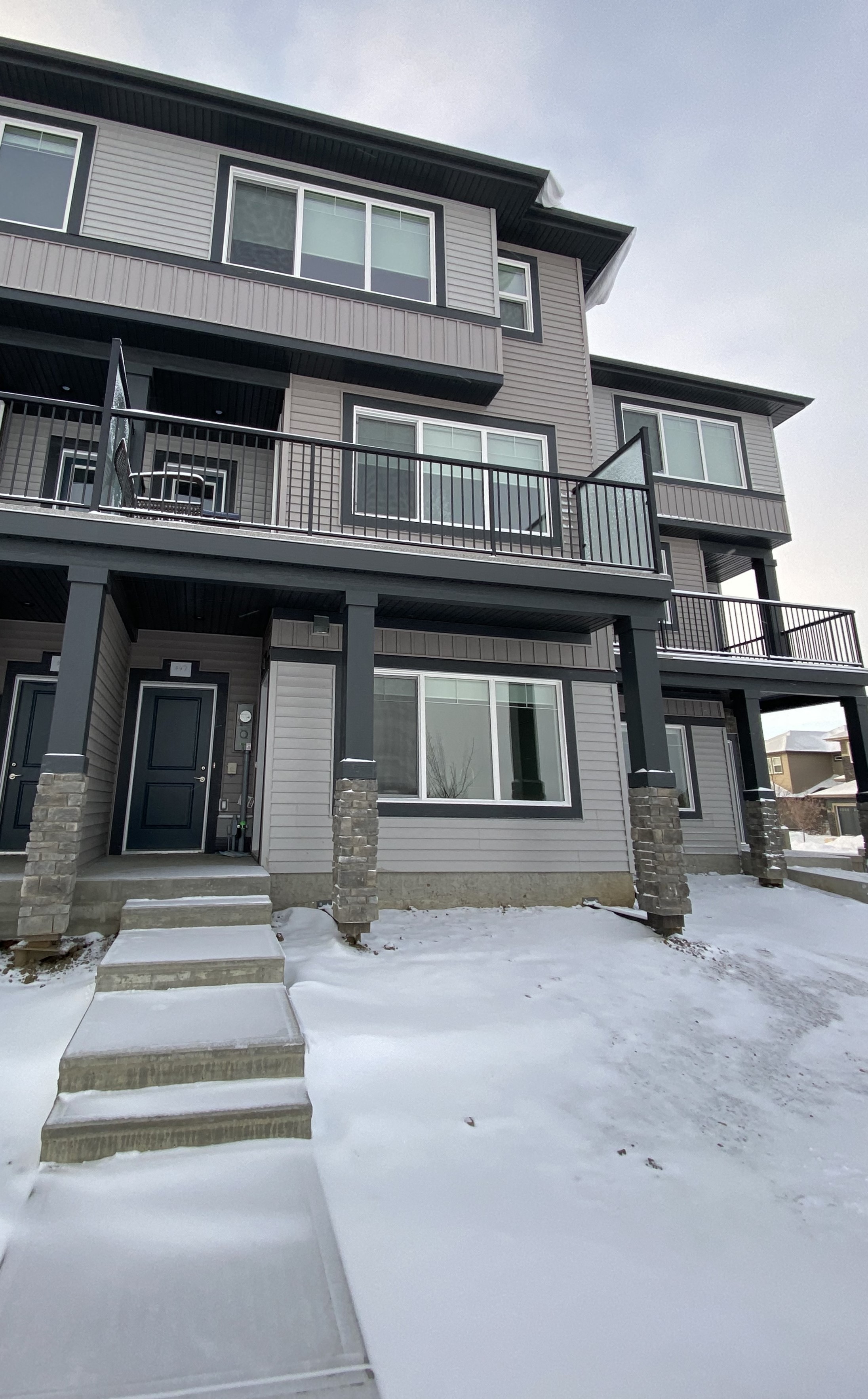 A snow-covered walkway leads to a two-story building with a balcony.